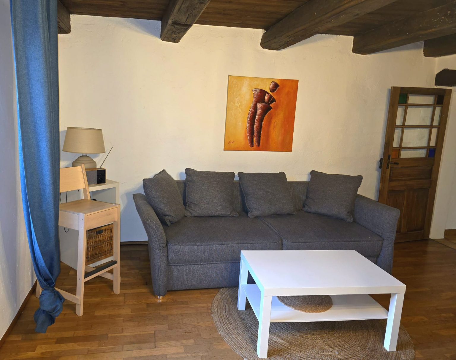 Wohnzimmer mit grauem Schlafsofa, Holzbalken und Fenster